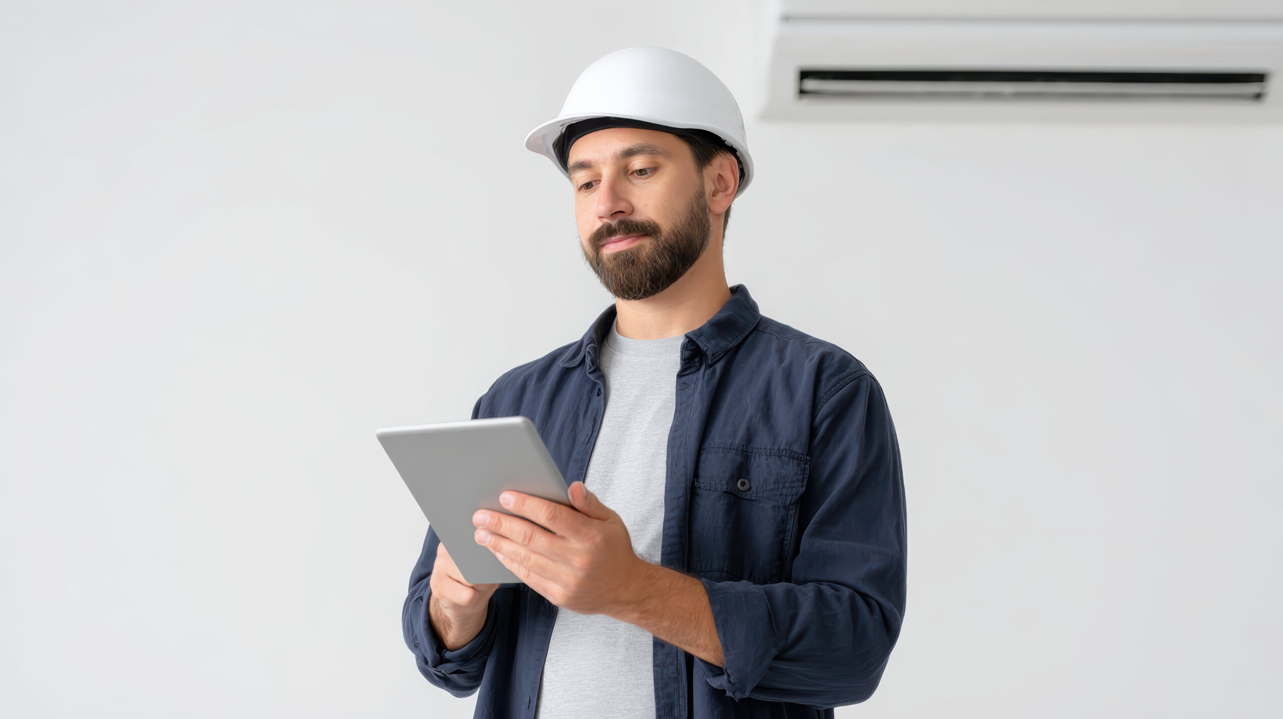 Focused male engineer and hvac technician performs repair and maintenance inspection on an air conditioner, documenting process on tablet. professional contractor works